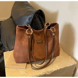 Close-up of brown suede tote bag featuring leather straps and gold metal ring hardware