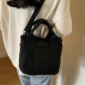 Black canvas tote bag for women featuring detachable strap and front pocket detail