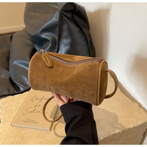 Close-up of brown suede cylinder bag with leather trim and silver zipper on stone base