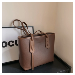 Detail of dark brown lychee textured leather tote bag with unique flap and leather tassels