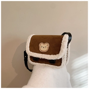 Détail du sac à bandoulière en daim marron avec garniture en peluche et écusson d'ours