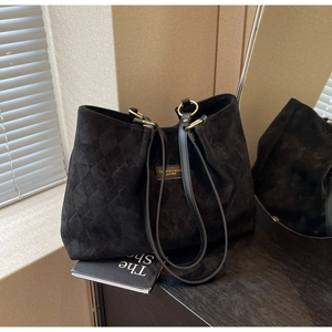 Detail of black suede tote bag featuring quilted diamond pattern and gold brand plaque