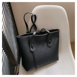 Detailed view of black litchi texture leather tote bag on a minimalist white chair