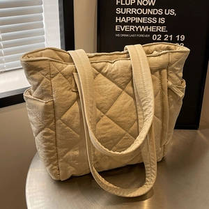 Quilted beige nylon tote bag with rhombus stitching and side pockets on a metal table
