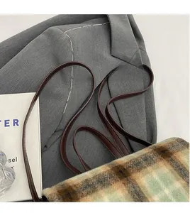 Detail of plaid shoulder bag with brown leather straps and autumn-themed texture