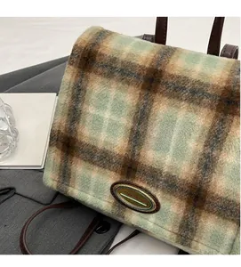 Close-up of green plaid wool fabric and metallic logo detail on a stylish backpack