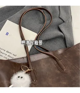 Macro detail of dark brown leather tote bag with long smooth straps and plush monster charm