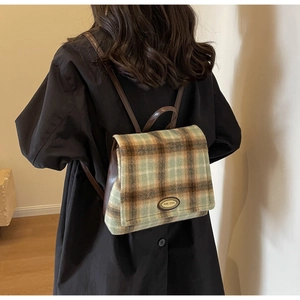 Detailed back view of a retro green tartan backpack featuring leather straps and metal plate