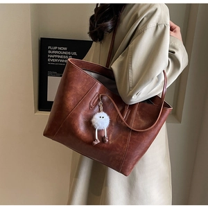 Detail of a large brown faux leather tote bag with a cute plush doll charm accessory