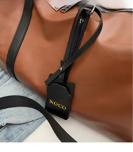 Detail of a brown leather travel bag with black handles and NOCO logo gold-stamped tag