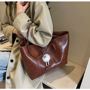 Brown vintage faux leather tote bag with white plush ball charm shown on shoulder