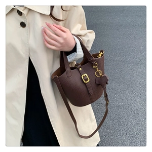 Detailansicht der braunen Bucket Bag aus Litschi-Leder mit goldener Schnalle und Anhänger