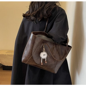 Retro deep brown tote bag with fuzzy white charm shown on shoulder for daily commute