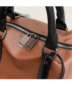 Detail of silver dual zippers and textured brown leather on a large travel bag
