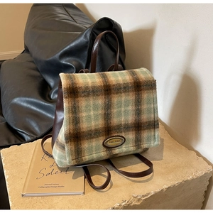 Close-up of retro plaid wool and brown leather backpack on a stone texture background