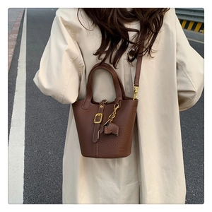 Detail of dark brown lychee leather bucket bag featuring a gold buckle and elephant charm