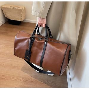 Close-up of a large brown cylinder travel bag with black handles and shoulder straps
