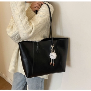 Detail of black leather tote bag with a cute white plush charm on a slim shoulder strap