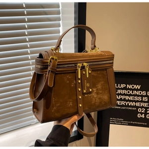 Detail einer dunkelbraunen Vintage-Tasche mit matten Texturen und goldenen Reißverschlüssen