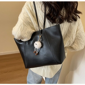 Detail of black textured tote bag with a white plush charm and long shoulder strap