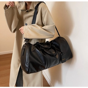 Close-up of black leather travel bag showing the removable wide fabric shoulder strap and tag