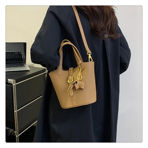 Detail der karamellbraunen Leder-Eimertasche mit Goldbeschlägen und Bogenanhänger