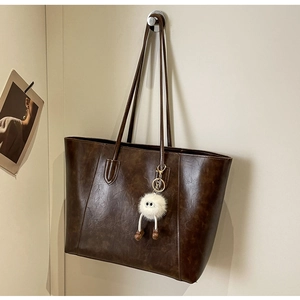 Detailed view of brown leather tote bag texture with cute plush monster keychain accessory