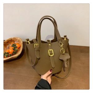 Detail der braunen Bucket Bag mit Litschi-Struktur, Golddekor und Elefantenanhänger
