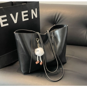 Detail of black leather tote bag with a cute white plush monster charm on a sofa