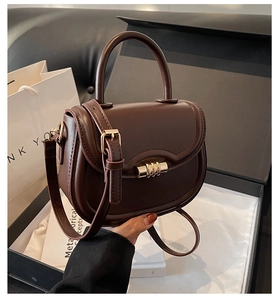 Detail of vintage coffee saddle bag with wave-edge flap and golden cylindrical lock