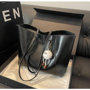 Close-up of large black tote bag with plush monster charm in elegant gift box