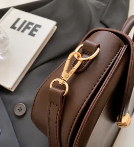 Detailed close-up of light gold metal hooks and stitching on a brown leather saddle bag