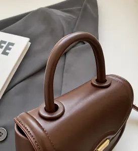 Detail of a dark brown leather handbag featuring a thick curved handle and matte finish