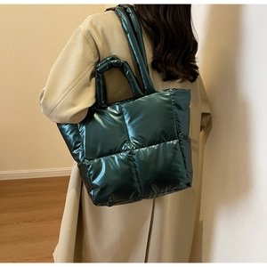 Dunkelgrüne gesteppte Shopper-Tasche im Daunenjacken-Stil getragen von einem Modell über Mantel