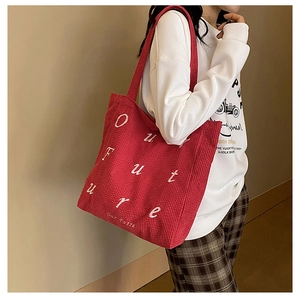 Side view of red corduroy tote bag with Our Future white embroidery on a model