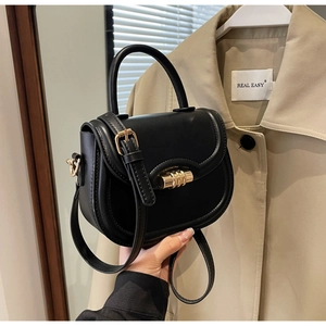 Detail of black leather saddle bag featuring a gold cylindrical lock and a top handle