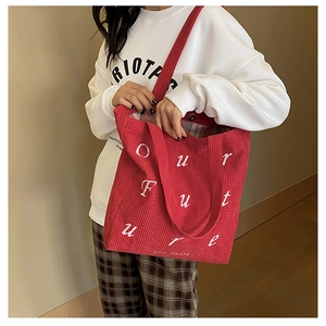 Detail of red corduroy tote bag showing Our Future embroidery and green plaid lining