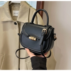 Detail of black leather saddle bag with golden cylindrical lock and sleek handle