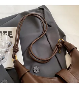 Detail of adjustable knotted shoulder strap and gold hardware on dark brown leather tote