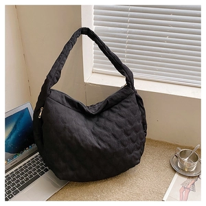 Close-up of black quilted canvas tote bag with textured scale pattern and gold zipper detail