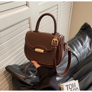 Detail view of dark brown leather saddle bag featuring a golden cylindrical metal lock clasp