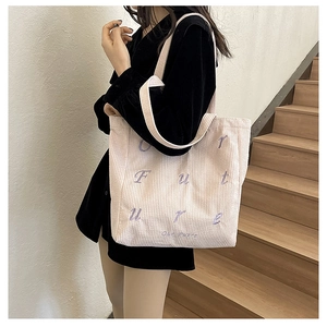Detail of corduroy tote bag with Future embroidery shown on model in stairwell