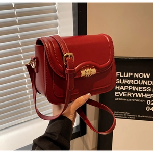 Detail of a deep red saddle bag featuring a distinctive triple gold bar lock and smooth finish