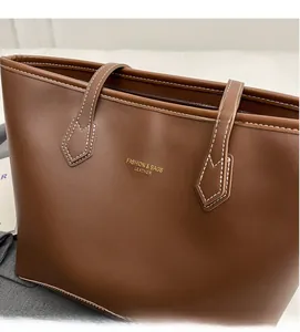 Gros plan d'un cabas en cuir marron avec logo doré et coutures apparentes soignées