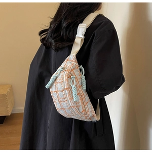 Detail of tweed crossbody chest bag with orange plaid pattern and blue woven zippers