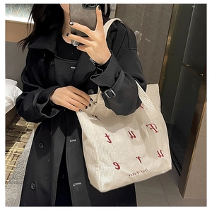 Detail of off-white corduroy tote bag featuring red letter embroidery and soft ribbed texture