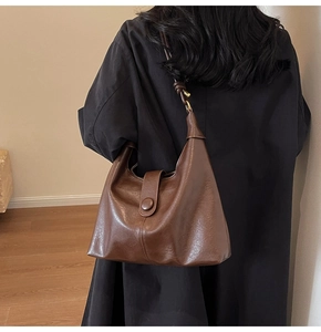 Brown leather tote bag with knotted strap detail shown on a model in a black coat