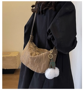 Détail du sac à bandoulière marron plissé avec pompon blanc et pendentif feuille