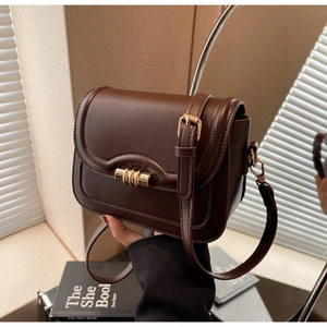 Detail of dark brown leather saddle bag featuring a gold cylindrical lock and matte texture