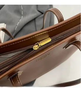 Détail de la fermeture éclair dorée et du logo sur le sac cabas en cuir marron